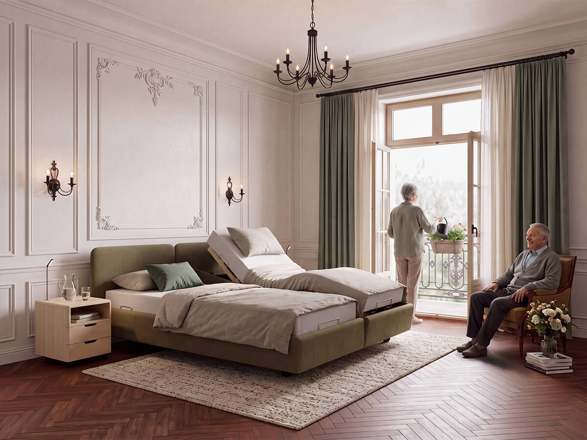 Polsterbett Cortina Classic von KIRCHNER mit salbeigrünem Polster, hochgestelltem Kopfteil und geneigtem Bettrahmen auf einer Seite in einem klassischen Schlafzimmer mit Stuckwänden; eine Frau gießt Blumen auf dem Balkon, ein Mann sitzt lächelnd im Sessel