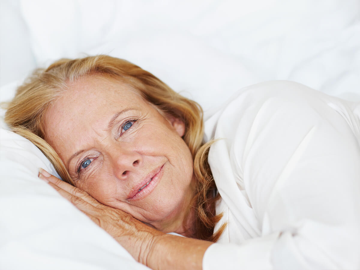 Seniorin lächelnd im Bett in komfortabler Seitenlage